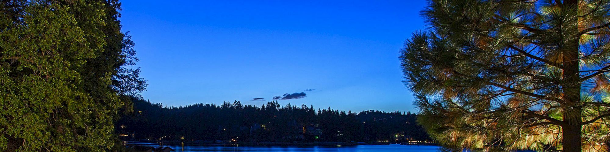 Lake Arrowhead at twilight with docked boats; chairs line a peaceful shore amidst trees.