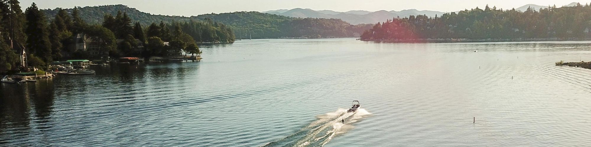 Lake Arrowhead with a boat, surrounded by forested hills under a clear sky.