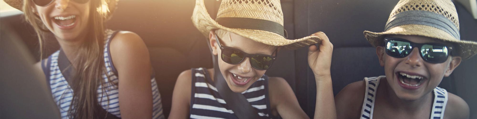 Three people in a car wearing straw hats and sunglasses are laughing happily.