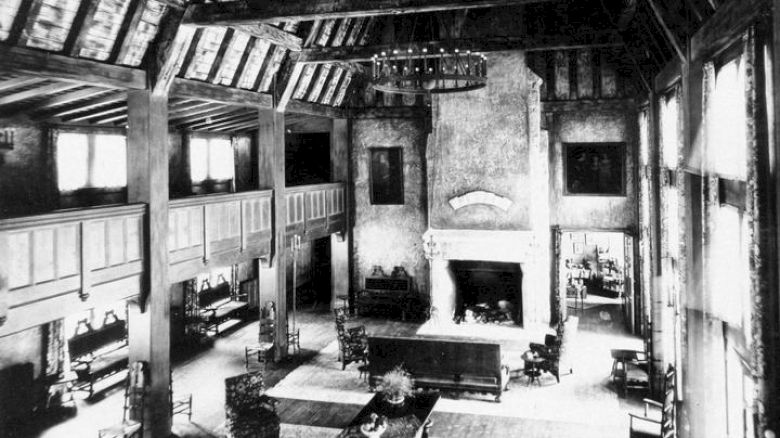 Vintage photo of Lake Arrowhead's Great Hall with a fireplace, timber beams, and sofas.