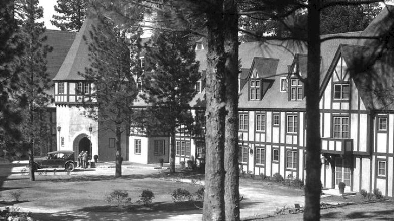 Vintage image of Lake Arrowhead's Tudor-style buildings with archway, surrounded by pine trees