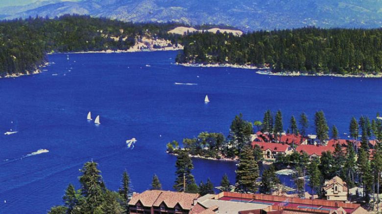 Historic aerial view Lake Arrowhead with boats, surrounded by forest and mountains.