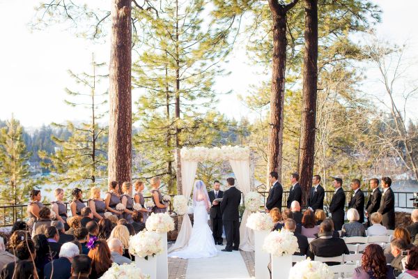 An outdoor wedding ceremony with guests, a couple at the altar, and scenic lake backdrop.