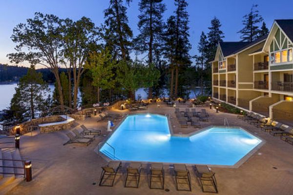 A tranquil pool by a lake adjacent to a hotel at dusk.