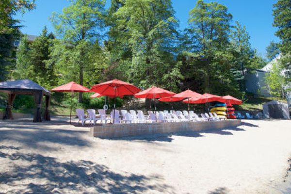 Outdoor seating with red umbrellas, white chairs on sand, surrounded by trees.