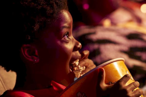 A child eating popcorn, watching a movie, looking up with an expression of awe.