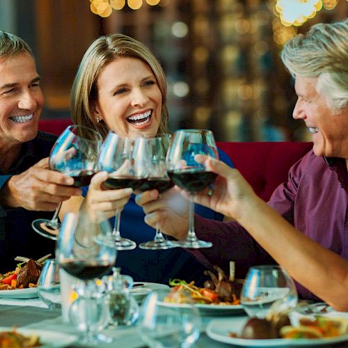 Four people are toasting with wine glasses at a dining table.