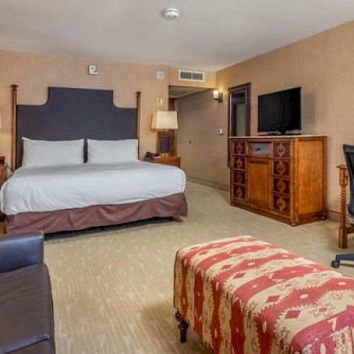 Hotel room with a bed, desk chair, dresser, and patterned bench.