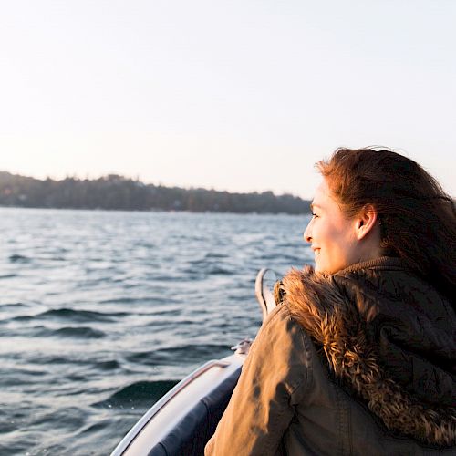 A woman is looking out to the water from a boat at sunset.