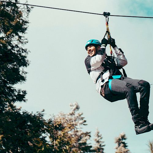 Person zip-lining amongst trees, smiling, with safety gear on.