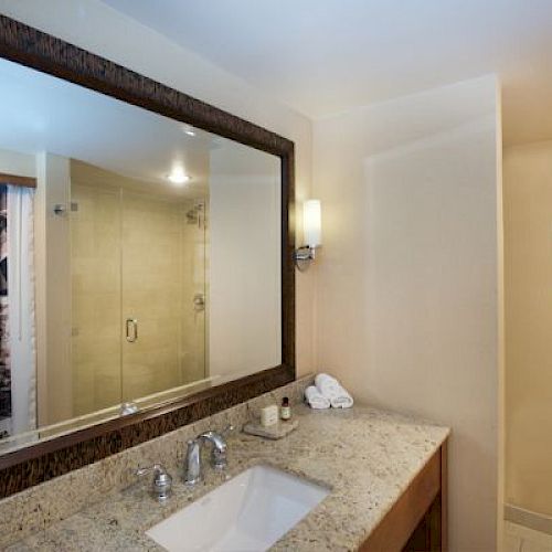 A modern bathroom with a large mirror, sink, towels, and a glass shower enclosure.