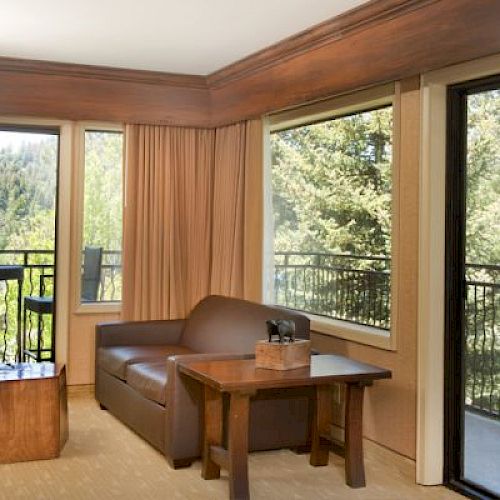 A cozy hotel living room with a sofa, table, and a view of trees through the balcony doors.