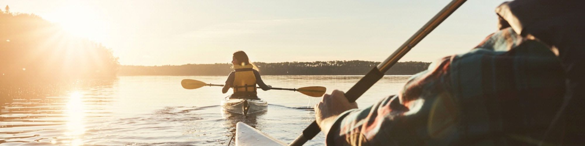 Two people are kayaking on a calm water surface at sunset.