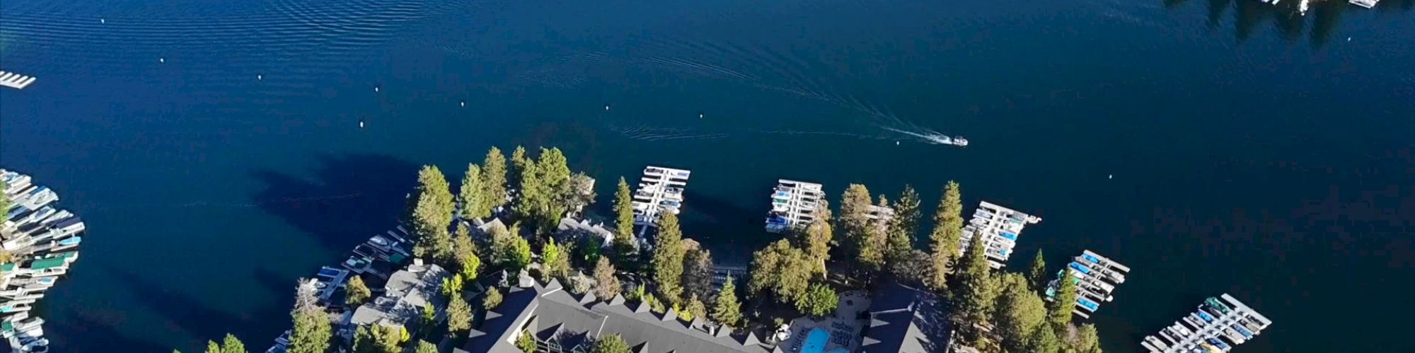 Aerial view of a lakeside area with buildings, docks, trees, and a boat.