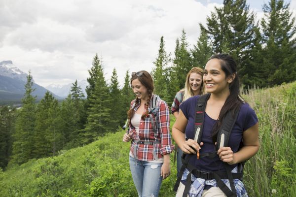 Three hikers smiling and walking on a trail with lush greenery and mountains in the background.