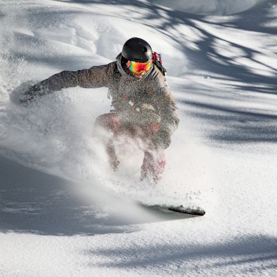 A person is snowboarding, carving through deep powder snow.