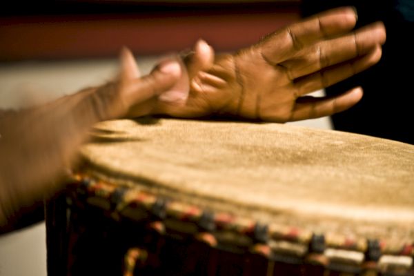 Hands playing a djembe drum, captured in motion.