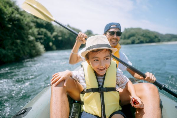 Two people in life jackets are smiling and kayaking on a river.