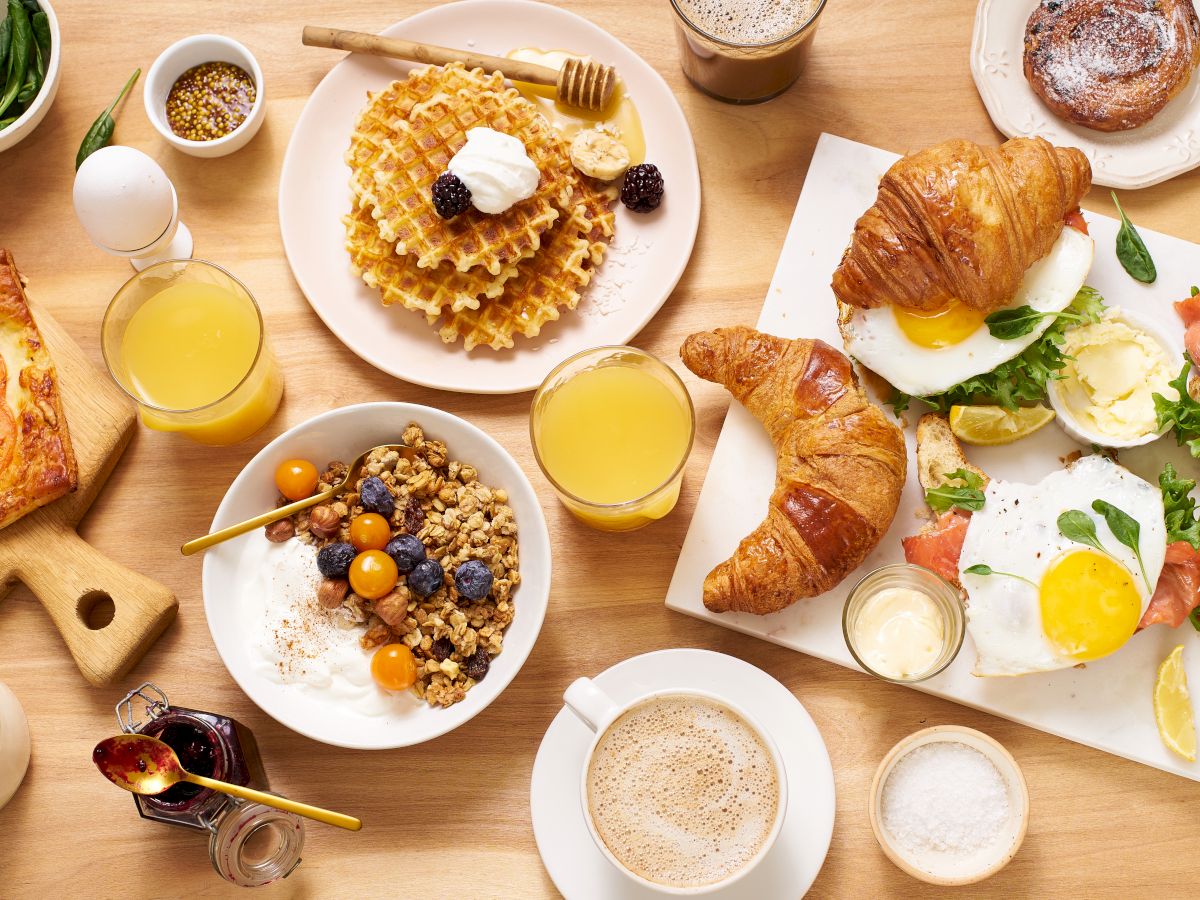 A table full of breakfast foods such as waffles, oatmeal, eggs, orange juice, and coffee.