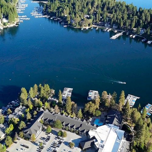 Aerial view of a serene lake surrounded by dense forests, with numerous docks and boats, and several buildings located near the water's edge.