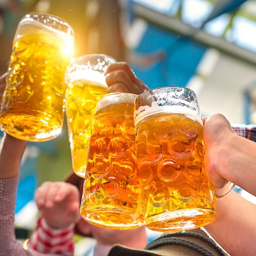 People raising large mugs of beer in a cheerful toast, with sunlight shining through the golden liquid.