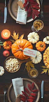 A Thanksgiving table setting with turkey, pumpkin pie, small pumpkins, fruits, colorful leaves, flowers, and plates with napkins.