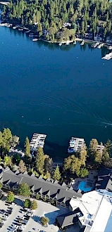 Aerial view of a lake surrounded by trees and docks, with buildings and boats visible. A serene, natural, and peaceful setting is depicted.