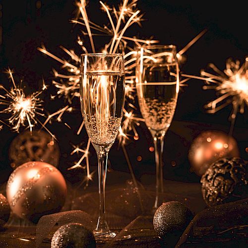 Two champagne glasses with sparklers, surrounded by ornaments and festive lights, creating a celebratory atmosphere.