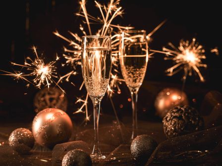 Two champagne glasses with sparklers and decorative baubles in a festive, dimly lit setting.