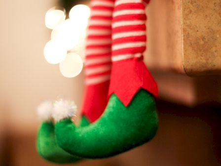 A pair of whimsical elf legs with red and white striped stockings and green shoes hanging from a ledge.