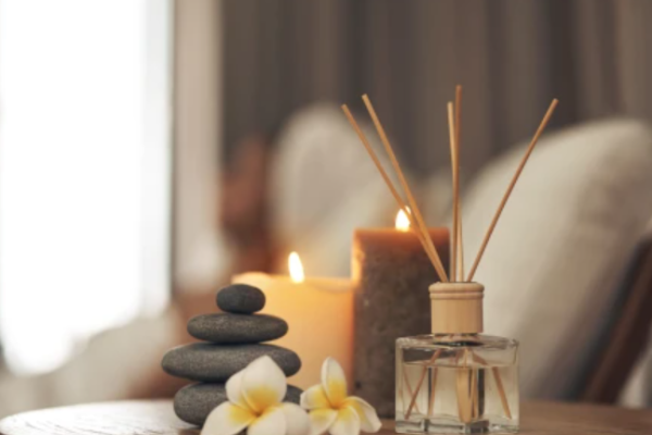 A tranquil scene with stacked stones, frangipani flowers, lit candles, and a reed diffuser on a wooden surface, creating a relaxing ambiance.