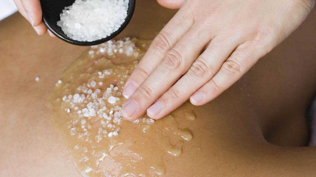 A person's back is being exfoliated with sea salt. The salt is being applied by hand in a relaxing spa setting.