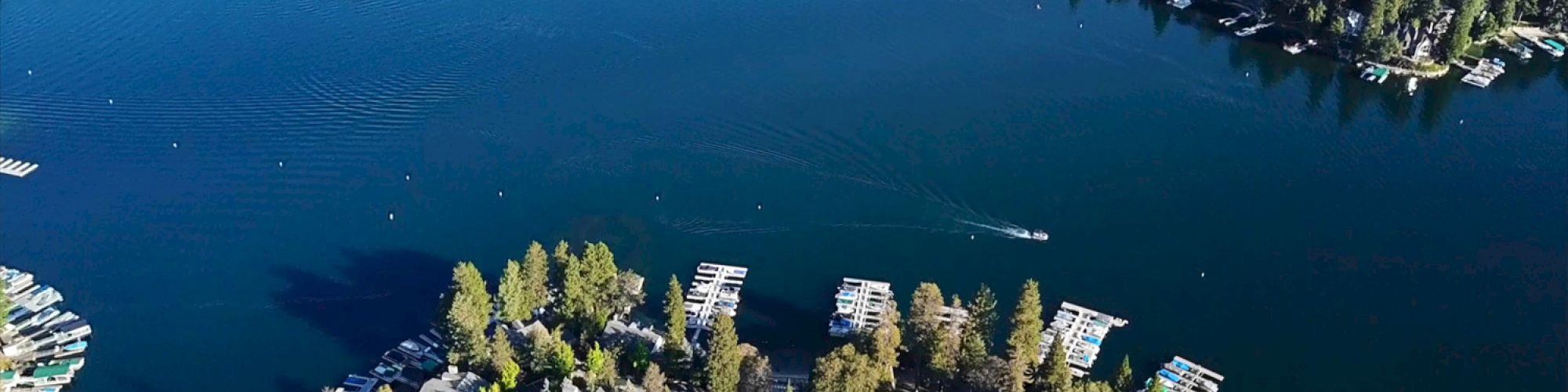 An aerial view of a scenic lake surrounded by dense forests, with docks and boats lining the shore, offering a tranquil, picturesque setting.