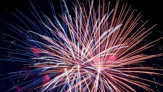 A vibrant burst of fireworks illuminates the night sky over a silhouetted landscape, adding vivid colors to the serene backdrop of dusk.