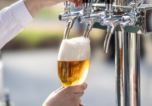 A person is pouring beer from a tap into a glass, creating a frothy head.