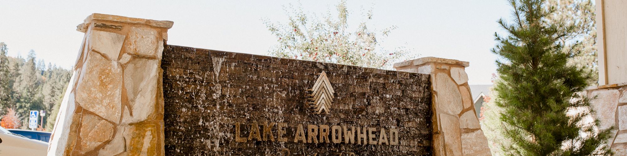 A stone sign with "LAKE ARROWHEAD Country Club & Golf Course" surrounded by plants and trees, under an open structure.