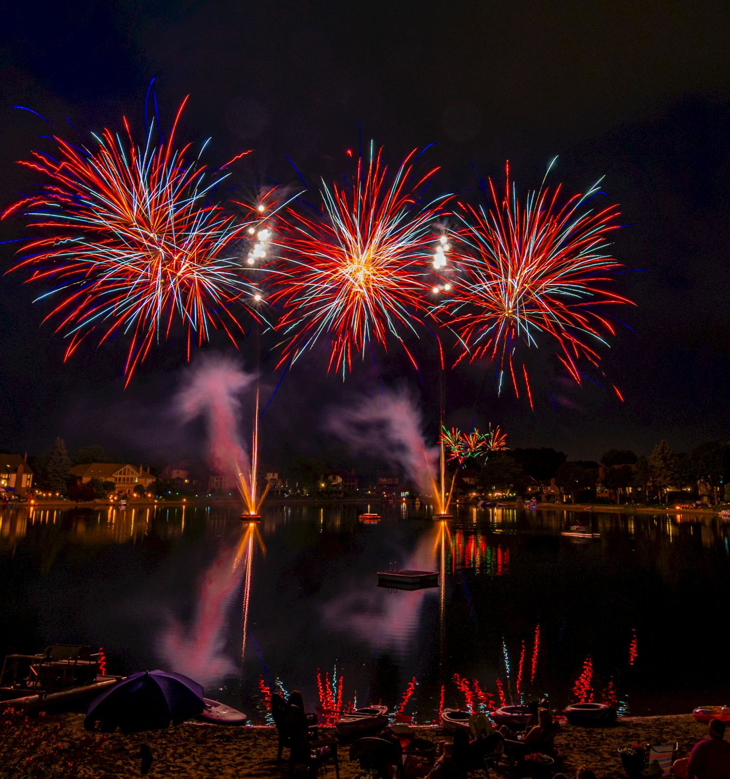 The image shows a night scene with vibrant fireworks exploding over a body of water, reflecting colorful lights.