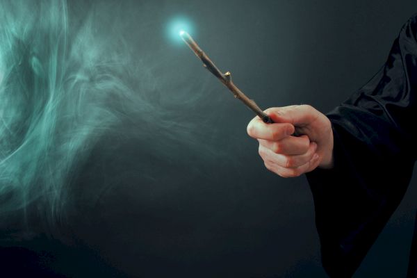A person holding a glowing wand with a misty, magical effect surrounding it against a dark background.